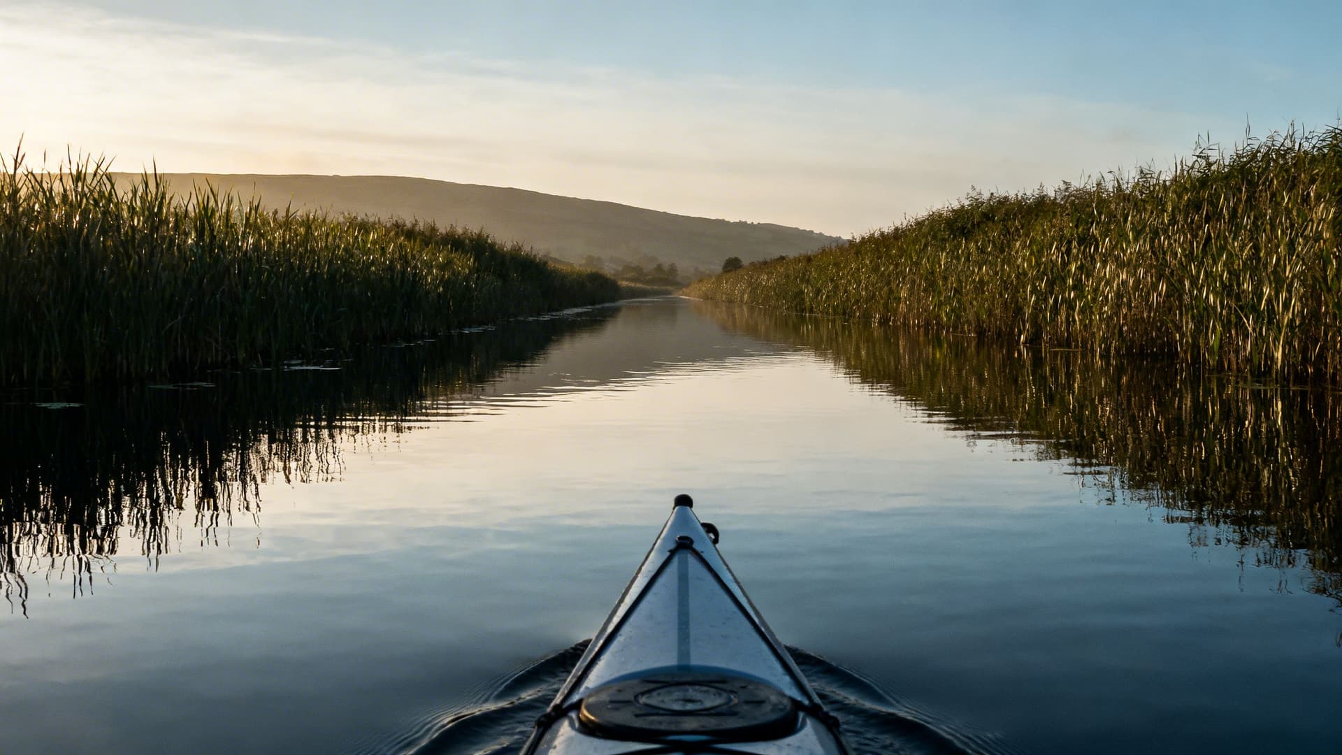A single kayak on the still water of the Shannon-Erne Blueway canal surrounded by reed beds and empty drumlin landscape in County Leitrim