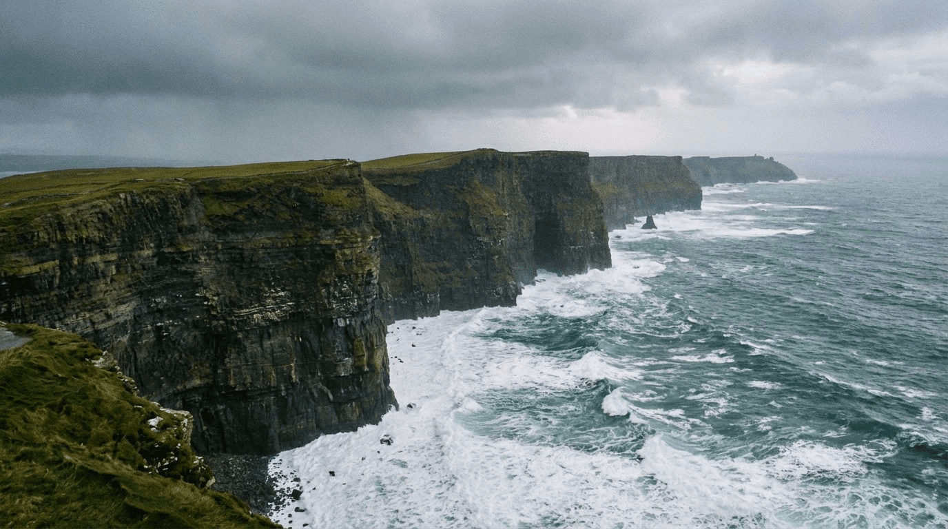 Dramatic aerial view of the Cliffs of Moher showing the sheer drop to the Atlantic, layered rock formations, waves crashing at the base, overcast dramatic sky