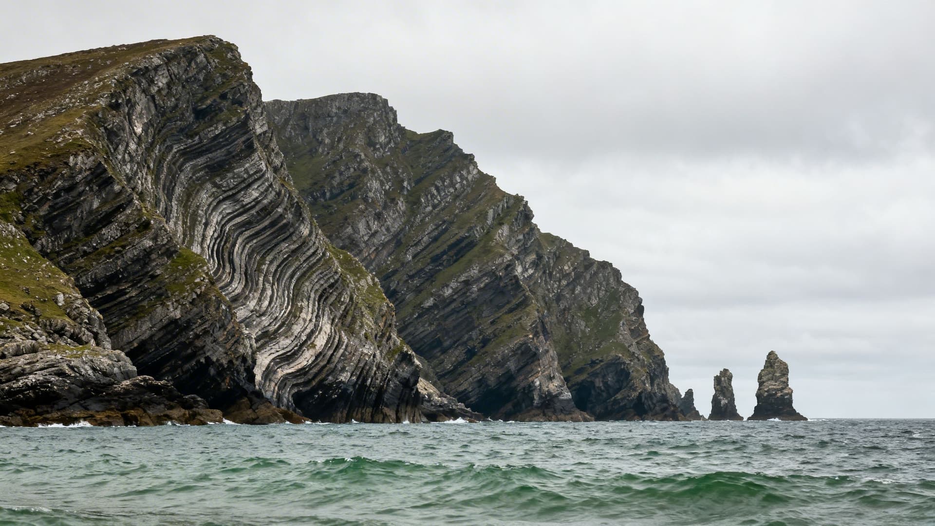 Looking north along Donegal's dramatic northwest coastline from the water, showing the broken series of headlands, sea stacks, and inaccessible cliff faces that make up Ireland's most remote Atlantic shore