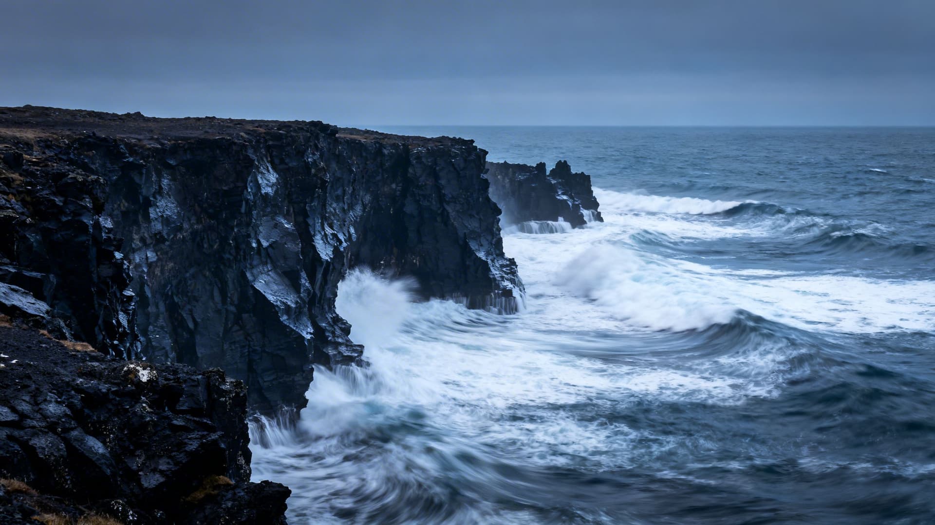Atlantic groundswell breaking at the base of Irish sea cliffs in January, white water against dark rock, dramatic winter light