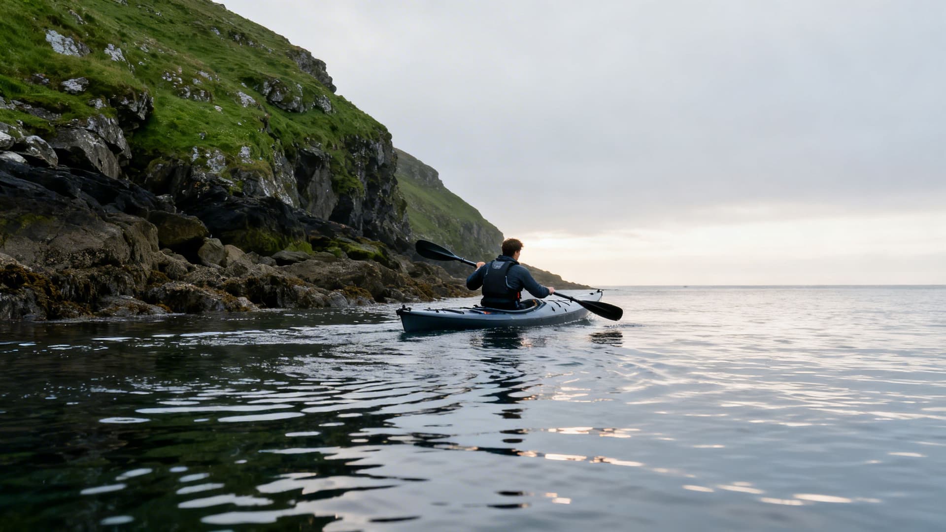 Beginner sea kayaker taking first cautious paddle strokes on calm Irish coastal water, learning balance and forward stroke technique
