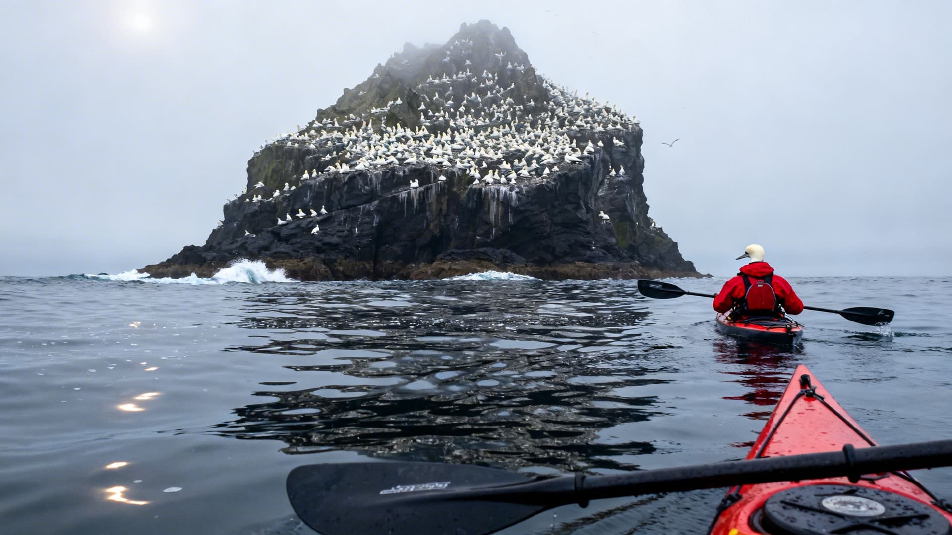 A sea kayaker approaching Skellig Michael across open Atlantic water, the monastic rock rising dramatically from the sea