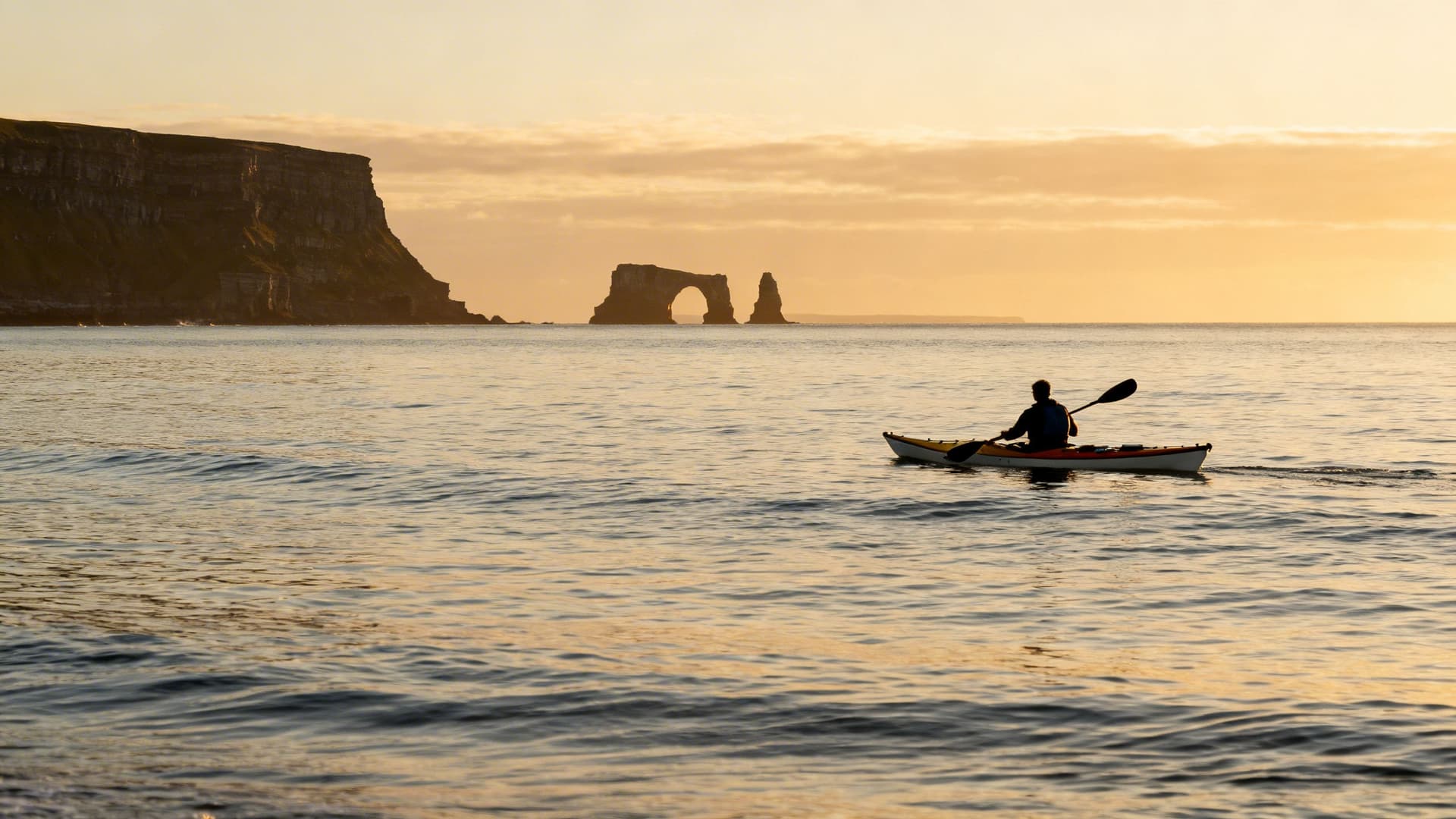 Sea kayaker paddling south from Doolin along the Clare coast toward the Cliffs of Moher, sea arches visible in the foreground