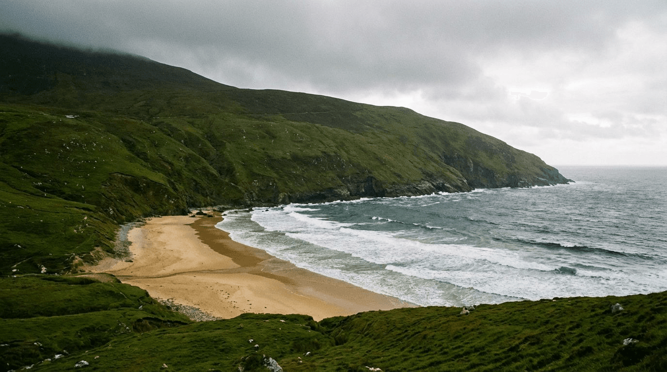 Keem Bay beach on Achill Island with golden sand crescent, steep green hills backdrop, dramatic Atlantic waves, overcast sky