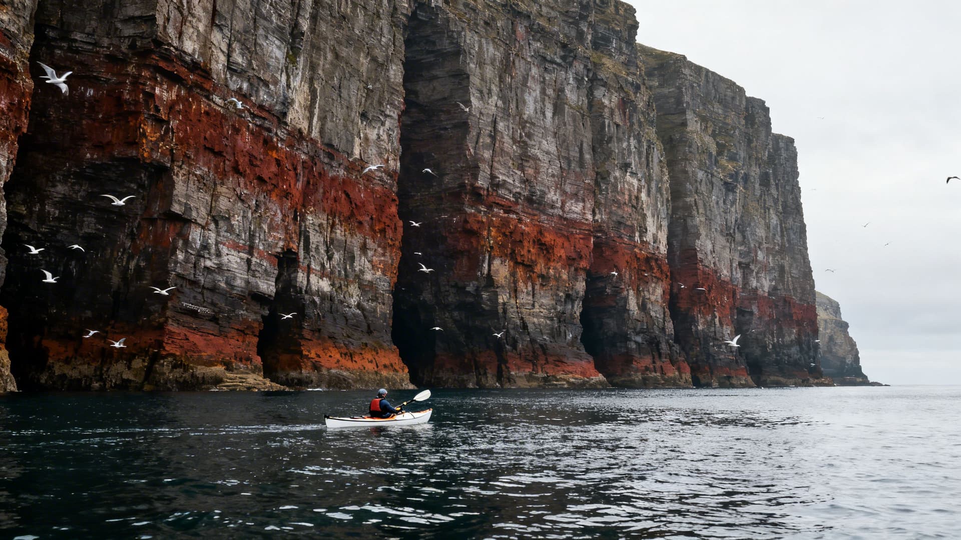 Sea kayaker at the base of Slieve League's 601-metre sea cliffs in County Donegal, the iron-stained rock face rising from the waterline into the sky above