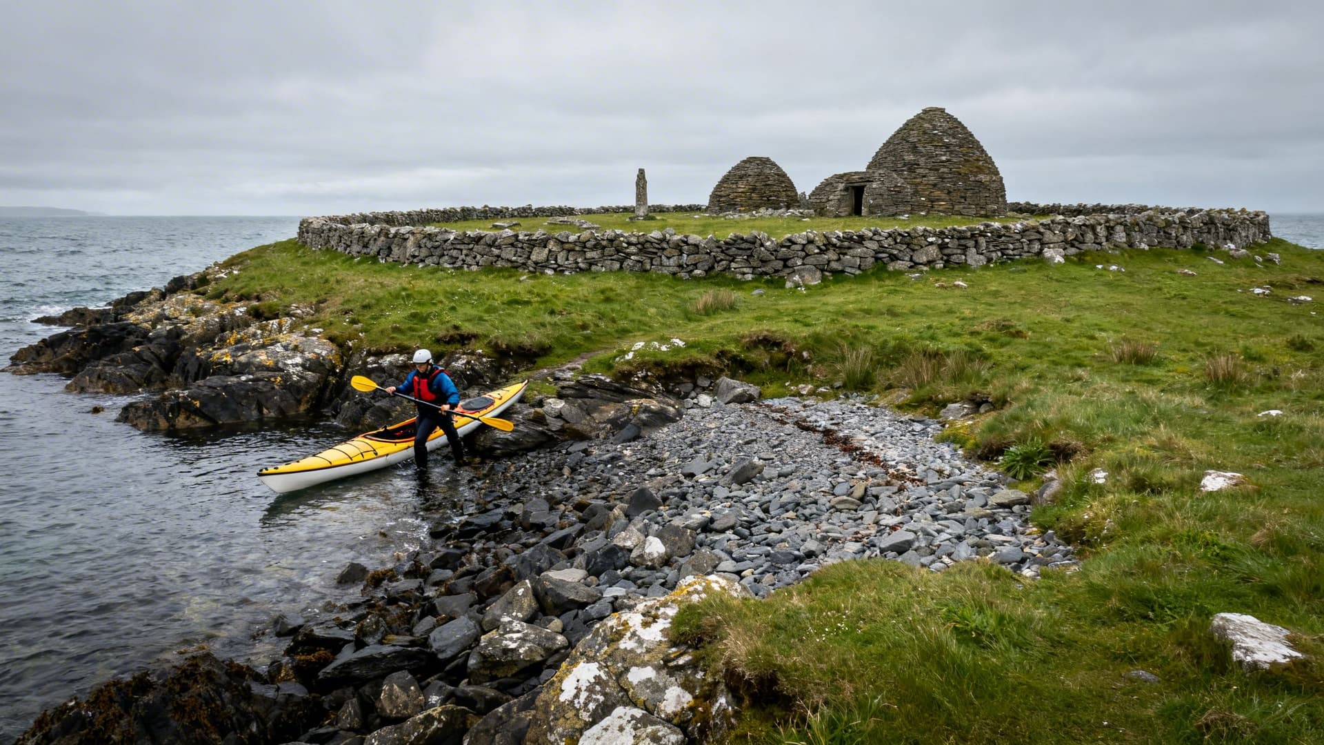 Stone cashel walls of the Inishmurray monastery complex on an uninhabited Atlantic island, the Sligo coast visible across open water in the distance