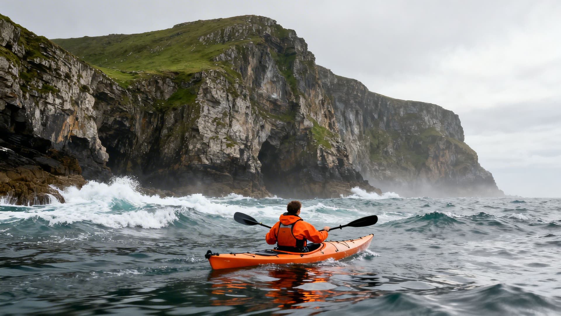 Donegal sea kayaking guide leading a small group along the base of the Atlantic-facing cliffs, pointing toward a cave entrance in the northwest Donegal coastline