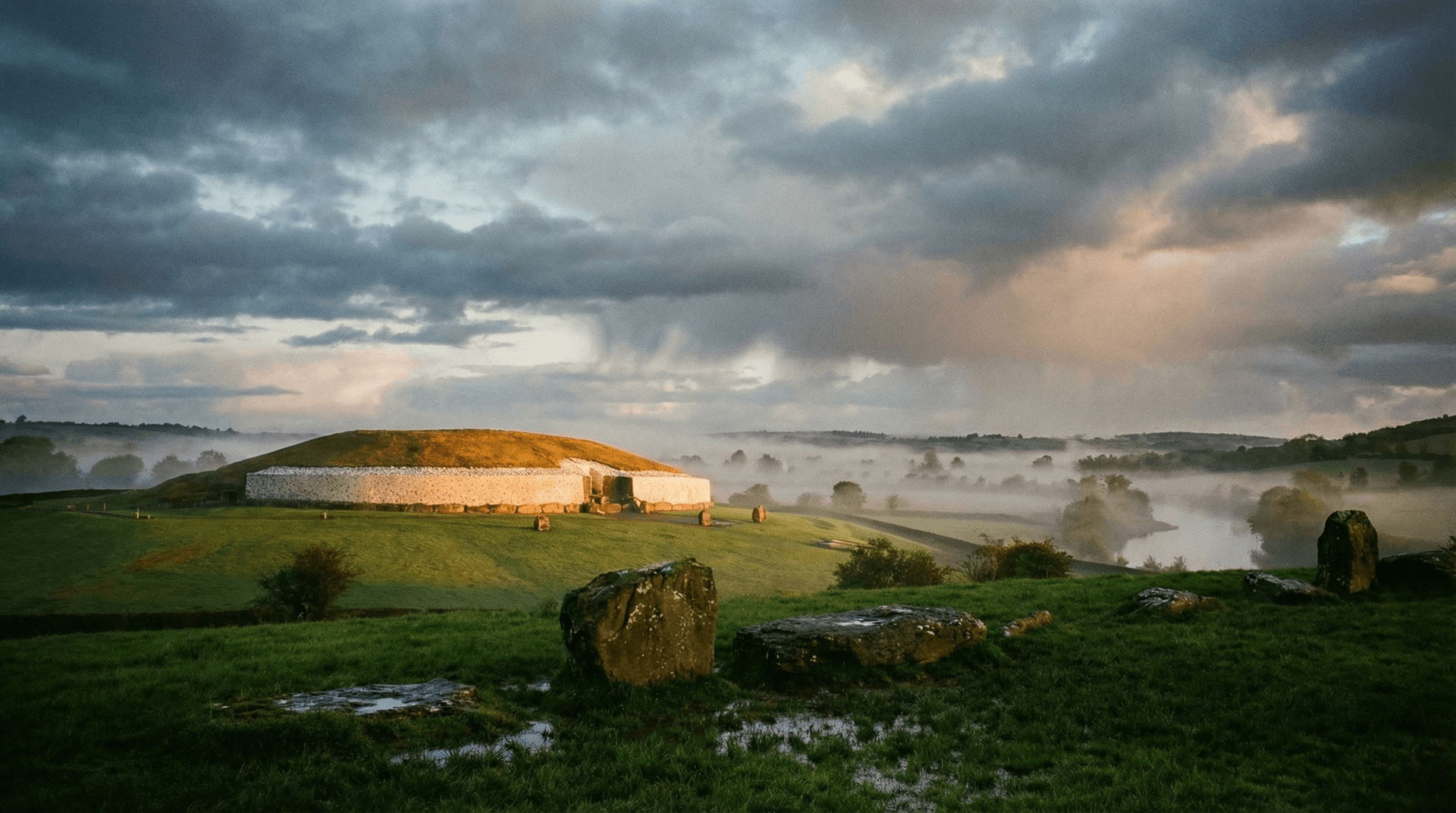 The white quartz facade of Newgrange passage tomb at dawn with mist rising from the Boyne Valley